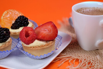 Primo piano di un piattino con paste alla frutta e tazzina di caffè su sfondo arancione