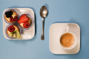 Vista dall'alto di un piattino con paste alla frutta, e una tazzina di caffè, sfondo celeste