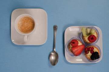 Paste alla frutta sul piatto e tazzina di caffè su sfondo celeste, vista dall'alto