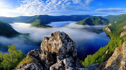 Obraz premium Misty morning landscape of a lake nestled in a valley, viewed from a rocky outcrop. The water is calm and surrounded by lush green vegetation. Soft