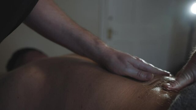 A man is massaging a woman's back. The man is wearing a black shirt and the woman is wearing a black shirt. Scene is relaxing and intimate