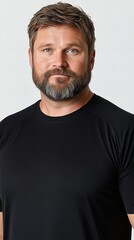 Obraz premium Portrait of a middle-aged Caucasian man with short brown hair and a beard, wearing a black t-shirt against a white background.