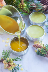 Pouring melted homemade pine needle salve balm into reusable tin container on white background.