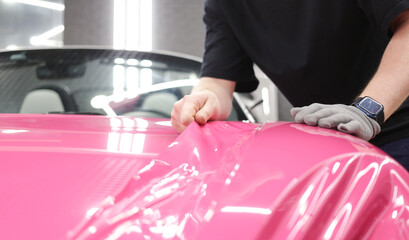 A specialist in wrapping a car with pink-colored vinyl film in the process of work. Car wrapping specialists cover the car with vinyl sheet or film. Car wrapping close-up. Selective focus.