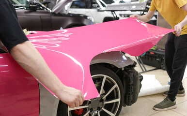 A specialist in wrapping a car with pink-colored vinyl film in the process of work. Car wrapping...