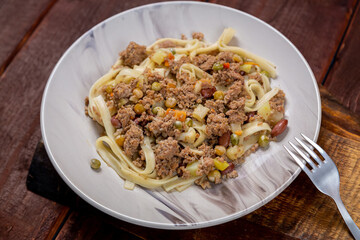 Noodles with minced meat and vegetables in sauce in a plate on the table next to a fork