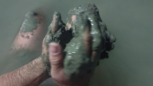 Man in a thermal wild lake applying volcanic healing mud to his body. Rupite, Bulgaria
