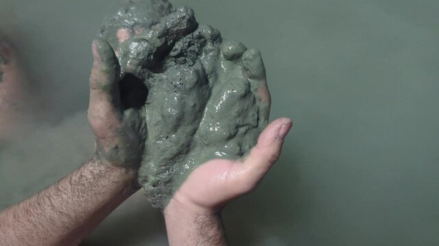 Man in a thermal wild lake applying volcanic healing mud to his body. Rupite, Bulgaria