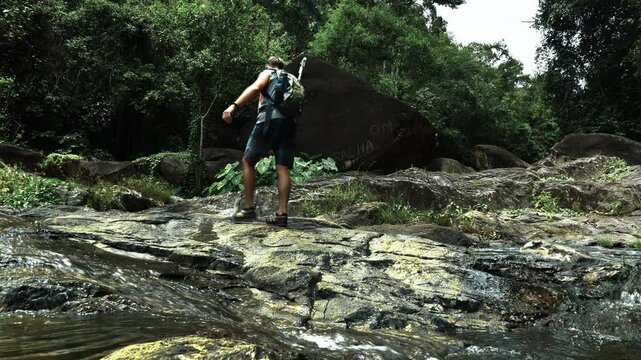 A tourist walks along a stone plateau, crossing a stream and comes to a giant stone