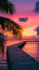 Fototapeta premium Wooden dock leading into the sea at sunset, with a vibrant sky and palm leaves framing the scene, symbolizing tranquility, beauty, and tropical escape