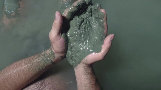Man in a thermal wild lake applying volcanic healing mud to his body. Rupite, Bulgaria