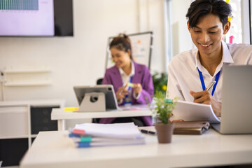 A group of people are sitting around a table with a laptop, a calculator, and a stack of papers. They are discussing business matters and looking at graphs and charts
