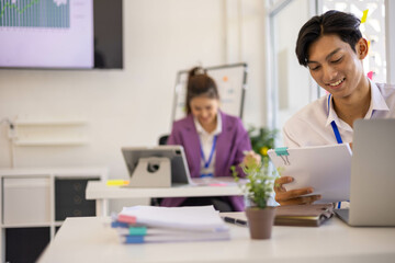 A group of people are sitting around a table with a laptop, a calculator, and a stack of papers. They are discussing business matters and looking at graphs and charts
