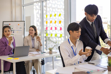 A group of people are sitting around a table with a laptop, a calculator, and a stack of papers. They are discussing business matters and looking at graphs and charts

