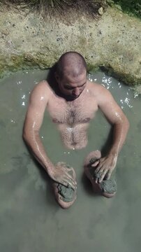 Man in a thermal wild lake applying volcanic healing mud to his body. Rupite, Bulgaria