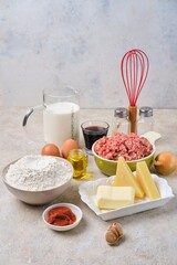 Prepared ingredients for cooking pancake lasagna or casserole with pancakes and minced meat on a light concrete background.