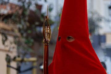 Close-up of a penitent wearing a red capirote, with only the eyes visible. The covered face contributes to the solemn atmosphere of the Holy Week procession, reflecting faith and devotion.