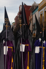 Three penitentes walk solemnly through the streets of Cabanyal during the Holy Week procession. Dressed in traditional robes and tall capirotes