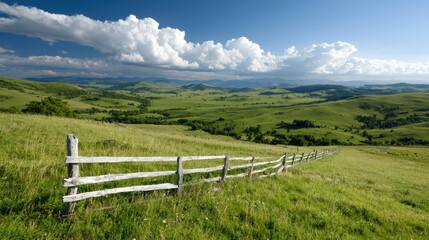 Fototapeta premium Wooden fence along rolling green hills stretches across a scenic countryside under a bright blue summer sky.
