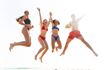 Happy friends jumping together on beach holding volleyball after winning match