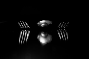 Two forks and spoon on black mirroring on a black backdrop. Close up shot. Food, restaurant, eating creative minimal design. 