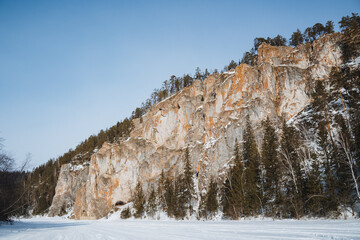A substantial and imposing rocky cliff stands tall, beautifully surrounded by trees draped in...