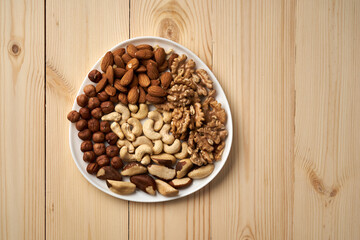 A plate of nuts with walnuts, cashews, almonds, and peanuts. The plate is on a wooden table
