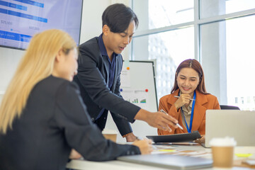 Three people are sitting at a table with a laptop open. One of them is laughing while the other two look on. The man in the middle is giving a presentation to the other two

