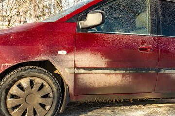 Dirty red car on a winter early morning, dirt stuck after driving on a winter city road. Close-up