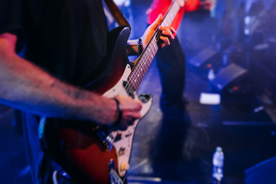 Concert view of an electric guitar player with vocalist and rock band performing in a club, male musician guitarist on stage with audience in a crowded concert show club hall arena, hands on a guitar