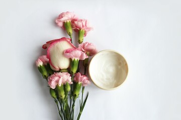 cosmetic cream and pink carnation flowers on white background, top view