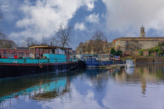 Tranquil reflections of colourful boats and leafless trees along the River Foss, York, North Yorkshire, UK.