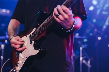Obraz premium Concert view of an electric guitar player with vocalist and rock band performing in a club, male musician guitarist on stage with audience in a crowded concert show club hall arena, hands on a guitar