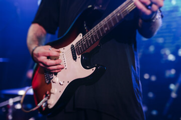 Obraz premium Concert view of an electric guitar player with vocalist and rock band performing in a club, male musician guitarist on stage with audience in a crowded concert show club hall arena, hands on a guitar