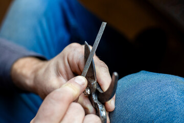 A man sharpens the blade of a garden pruner with a file. Garden tools