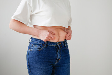 A woman can't fasten her jeans because she's overweight on a gray background