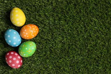 Beautiful decorated Easter eggs on green grass, flat lay. Space for text