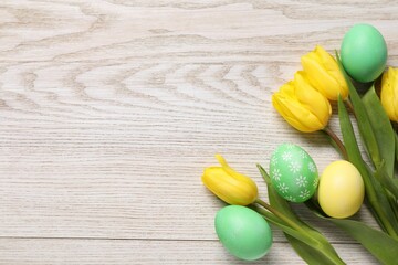 Easter eggs and beautiful tulips on wooden background, flat lay. Space for text