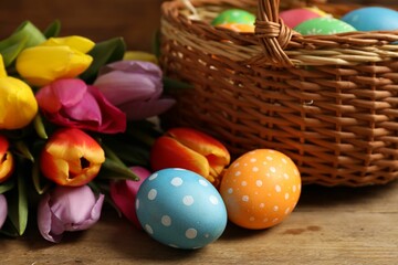 Easter eggs in wicker basket and beautiful tulips on wooden table, closeup