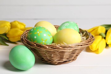 Easter eggs in wicker basket and beautiful tulips on white wooden table, closeup