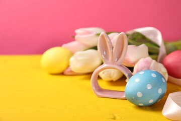 Easter eggs, beautiful tulips and bunny figure on yellow wooden table against pink background, closeup. Space for text