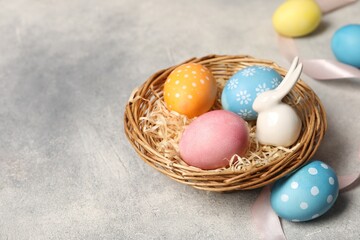 Easter eggs in wicker basket and bunny figure on grey table, closeup. Space for text