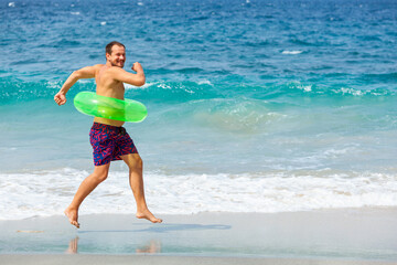 Happy bearded hipster in inflatable ring have fun on beach walk. Funny man run along sea surf and...