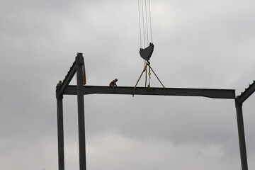 A construction worker on a steel beam in the heights while it is being transported by a construction crane. A man working in the construction.