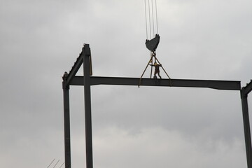 A construction worker on a steel beam in the heights while it is being transported by a construction crane. A man working in the construction.