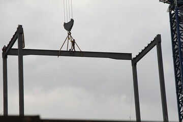 A construction worker on a steel beam in the heights while it is being transported by a construction crane. A man working in the construction.