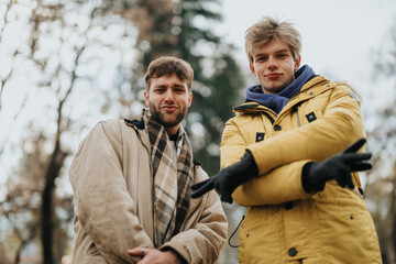 Two young men wearing jackets and making confident poses together during a brisk autumn day...