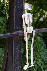 A skeleton is hanging from a bridge rail. The skeleton is white and has red nails. Scene is eerie and spooky