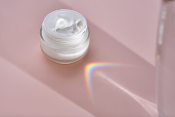 An open jar of cream with its texture on a pink background.