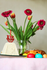 Orthodox easter table setting with colorful eggs, traditional cake paska bread, kulich,  cheese paskha, burning candle, fresh flowers, and festive decor 
